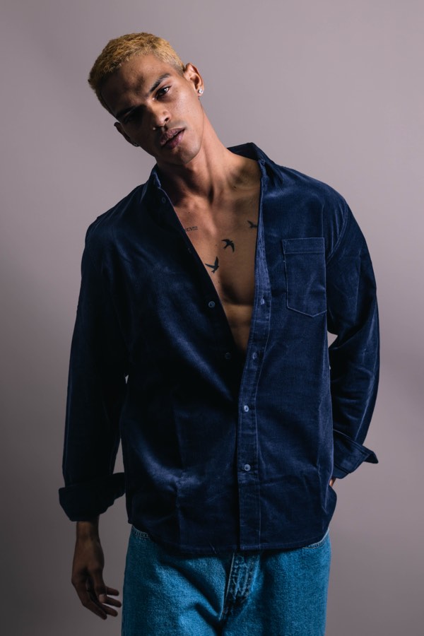Male model in an open navy corduroy shirt with rolled sleeves, editorial studio portrait