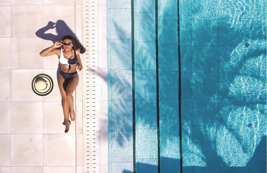 Aerial view of a woman lying poolside in a black and white swimsuit, styled lifestyle content shoot