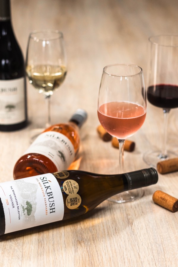 Silkbush wine bottles and glasses of red, rosé and white wine styled on a wooden table